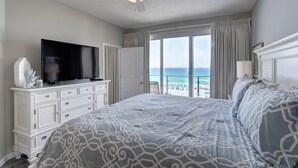 Quarto com uma cama grande, televisão, ventilador de teto e vista para o oceano.