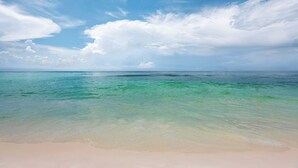 Uma praia com águas turquesa cristalinas e uma faixa de areia dourada sob um céu parcialmente nublado.