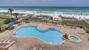 Uma piscina com espreguiçadeiras e guarda-sóis, uma praia com espreguiçadeiras e guarda-sóis, e vista para o oceano.