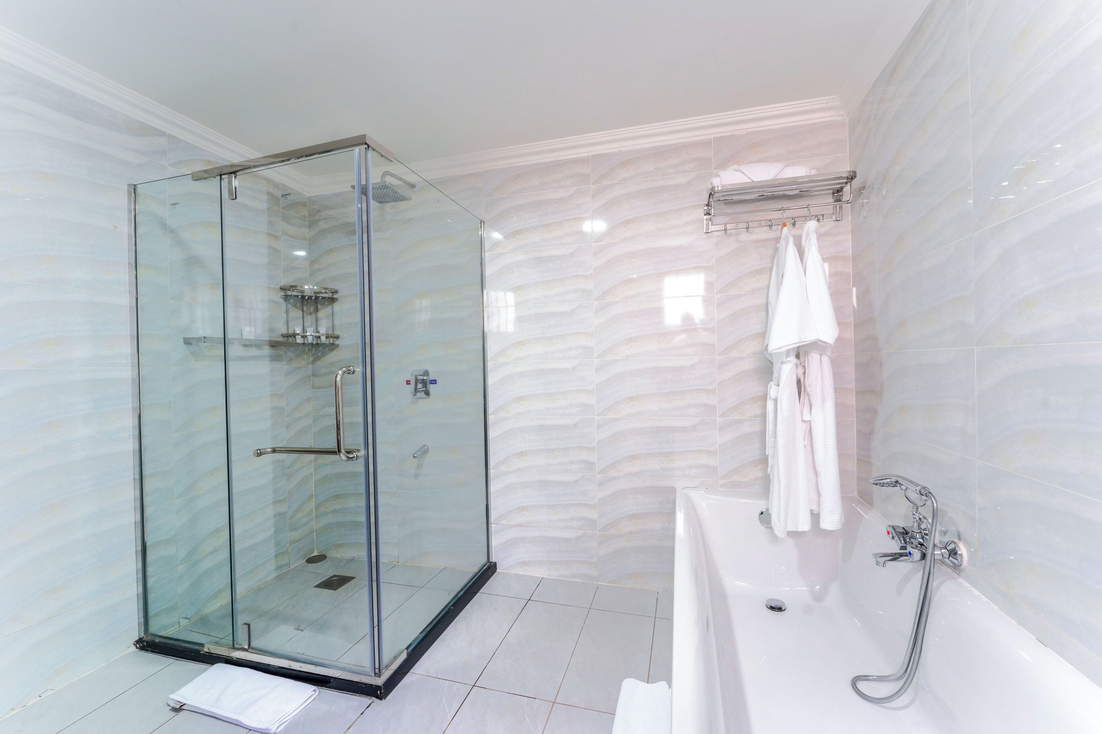 A modern bathroom with a glass-enclosed shower, a white bathtub, and a marble-patterned wall.