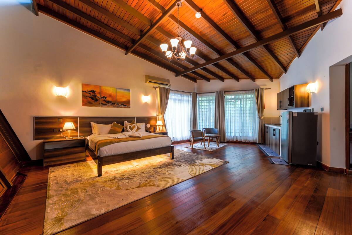 Um quarto espaçoso com uma cama grande, piso de madeira, um candelabro e vista para o exterior por grandes janelas.