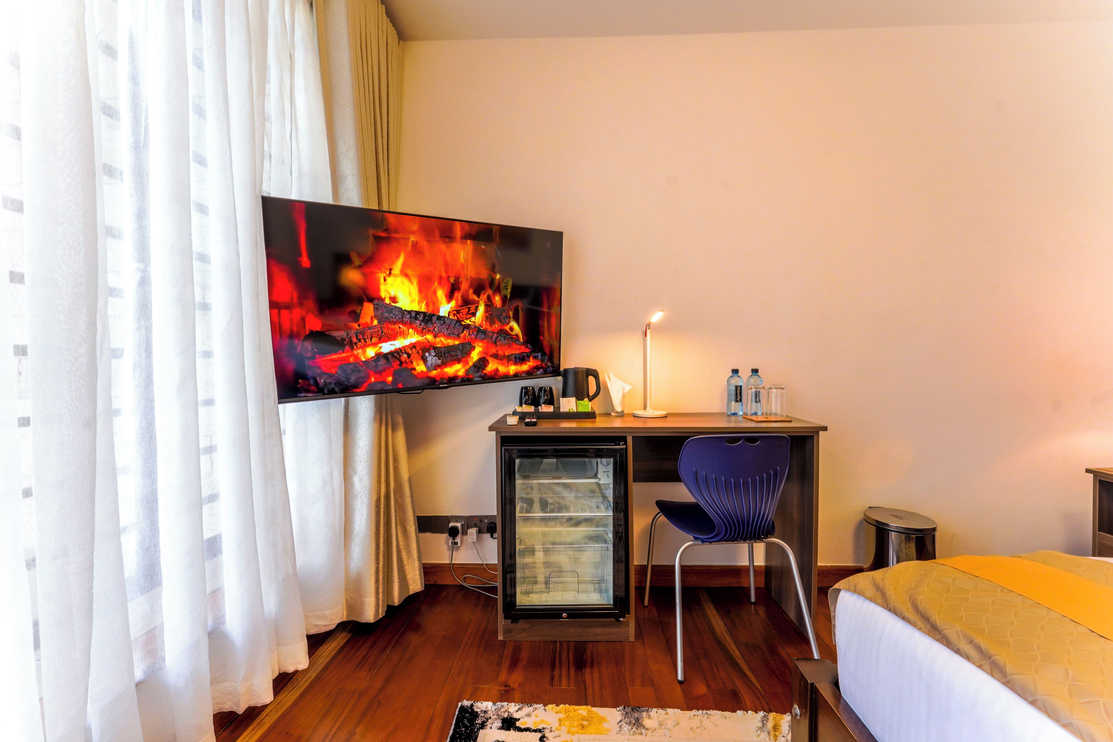 Une chambre d’hôtel comprenant un lit, un bureau avec un ordinateur, un téléviseur diffusant une image de cheminée et une chaise.