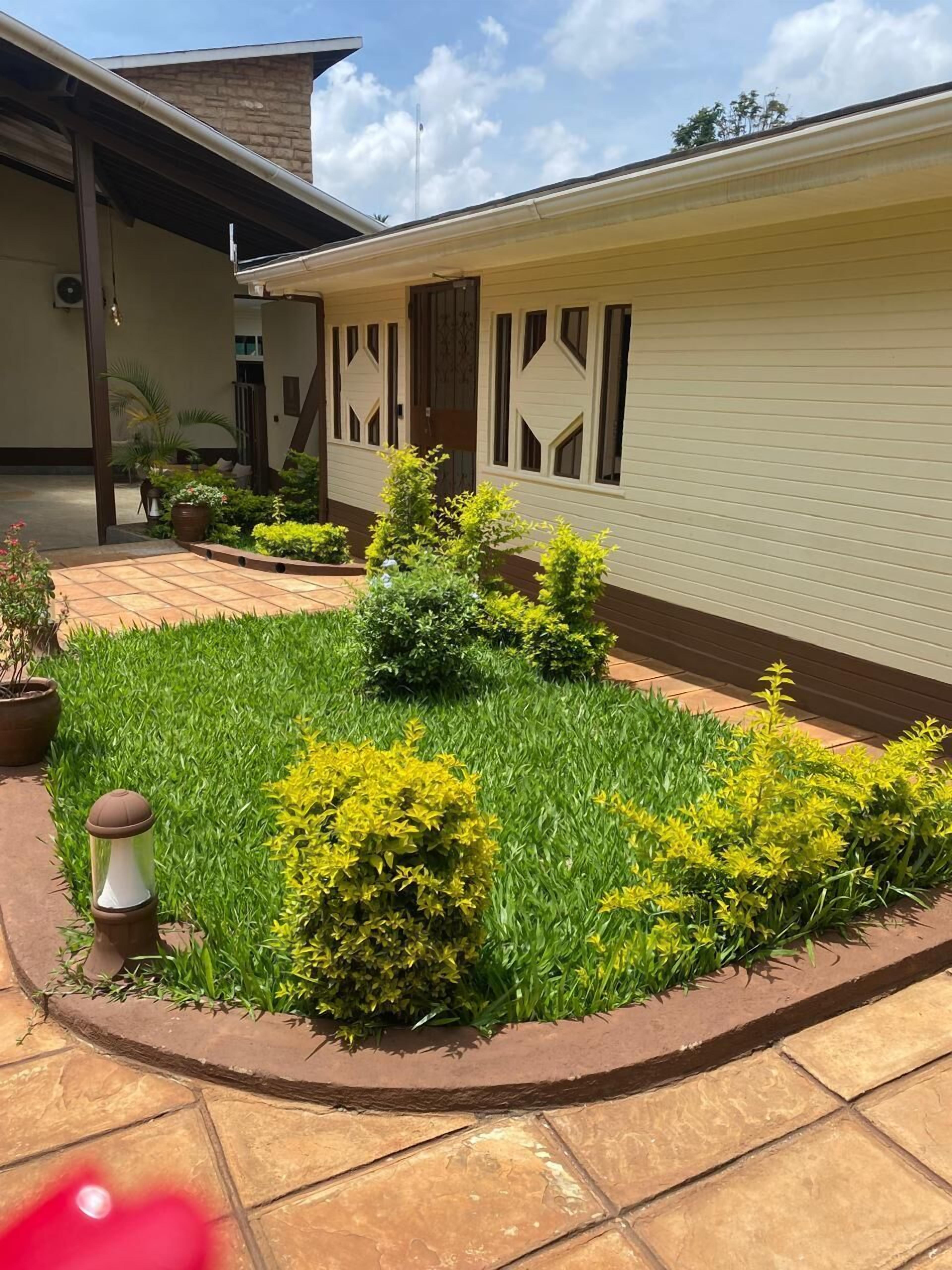A building with a covered entrance, a garden with green grass and yellow shrubs, and a tiled patio area.