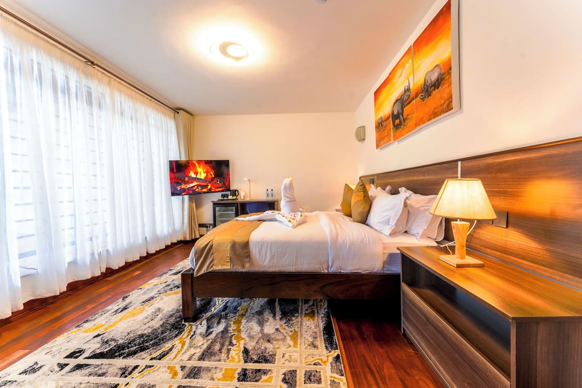 Quarto de hotel com cama, televisão, mesa de cabeceira com luminária e um quadro na parede.