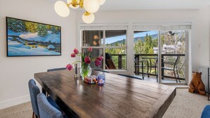 A dining area with a wooden table, chairs, a vase with flowers, and a painting on the wall. - Elegant tranquility spacious 3BR golf course views close to Village & Lost Lake (Whistler)