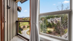 A room with a large window, a view of a house, and a hanging bird feeder. - Elegant tranquility spacious 3BR golf course views close to Village & Lost Lake (Whistler)