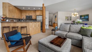 A modern kitchen with wooden cabinets, a bar area, and a seating area with a grey sofa and a wooden coffee table. - Elegant tranquility spacious 3BR golf course views close to Village & Lost Lake (Whistler)