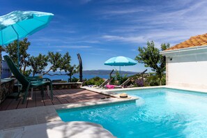 A pool area with lounge chairs and umbrellas, a view of the sea, and a stone deck. - Villa Kety with Pool -Seaview (Makarska)