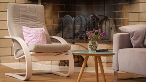 A modern living room with a stone fireplace, a beige recliner with a pink pillow, a glass coffee table, and a grey sofa.