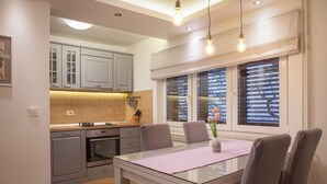 A modern kitchen with grey cabinets, a glass dining table, and pendant lighting.