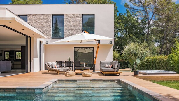 Een modern huis met een zwembad, tuinmeubilair en een patio.
