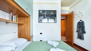 Ein Hotelzimmer mit einem Bett, einer grünen gesteppten Bettdecke, zwei aufgerollten Handtüchern, einem gerahmten Bild an der Wand und einem Holzschrank.
