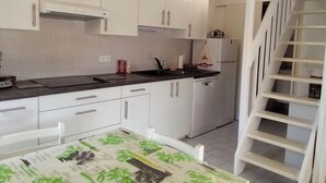 A kitchen with white cabinets, a black countertop, and a stainless steel sink. There is a white chair and a table with a green tablecloth. A white staircase is visible to the right.