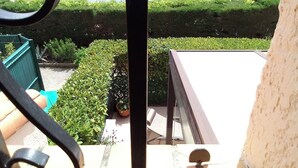 A view from a balcony overlooking a courtyard with a pool, neatly trimmed hedges, and a staircase.