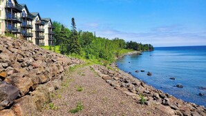 A coastal hotel with multiple balconies, a rocky shoreline, and a clear view of the sea. - Lakefront Condo: Pool, Hot Tub, Deck, Fireplaces (Two Harbors)