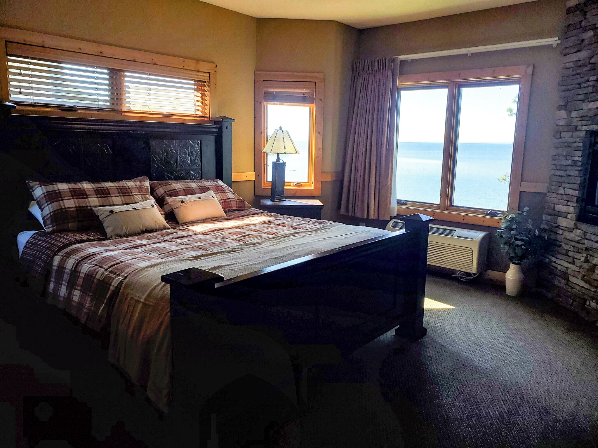 Una camera da letto con un letto, un comodino, una lampada, una finestra con tende e vista sul mare.