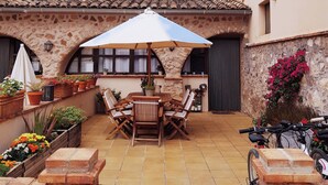 Une terrasse extérieure avec une table et des chaises, entourée de plantes en pot et d’un mur de pierre.