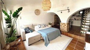 Une chambre à coucher comprenant un lit, un canapé, une plante en pot, une horloge et une porte en arc donnant sur une cuisine.