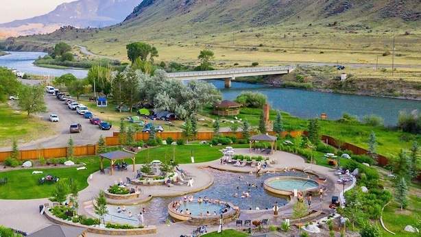 Un resort con varias piscinas, un puente sobre un río y montañas al fondo.