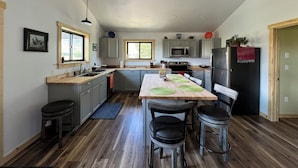 Una cocina moderna con gabinetes grises, un refrigerador negro y una mesa de comedor de madera con cuatro sillas.