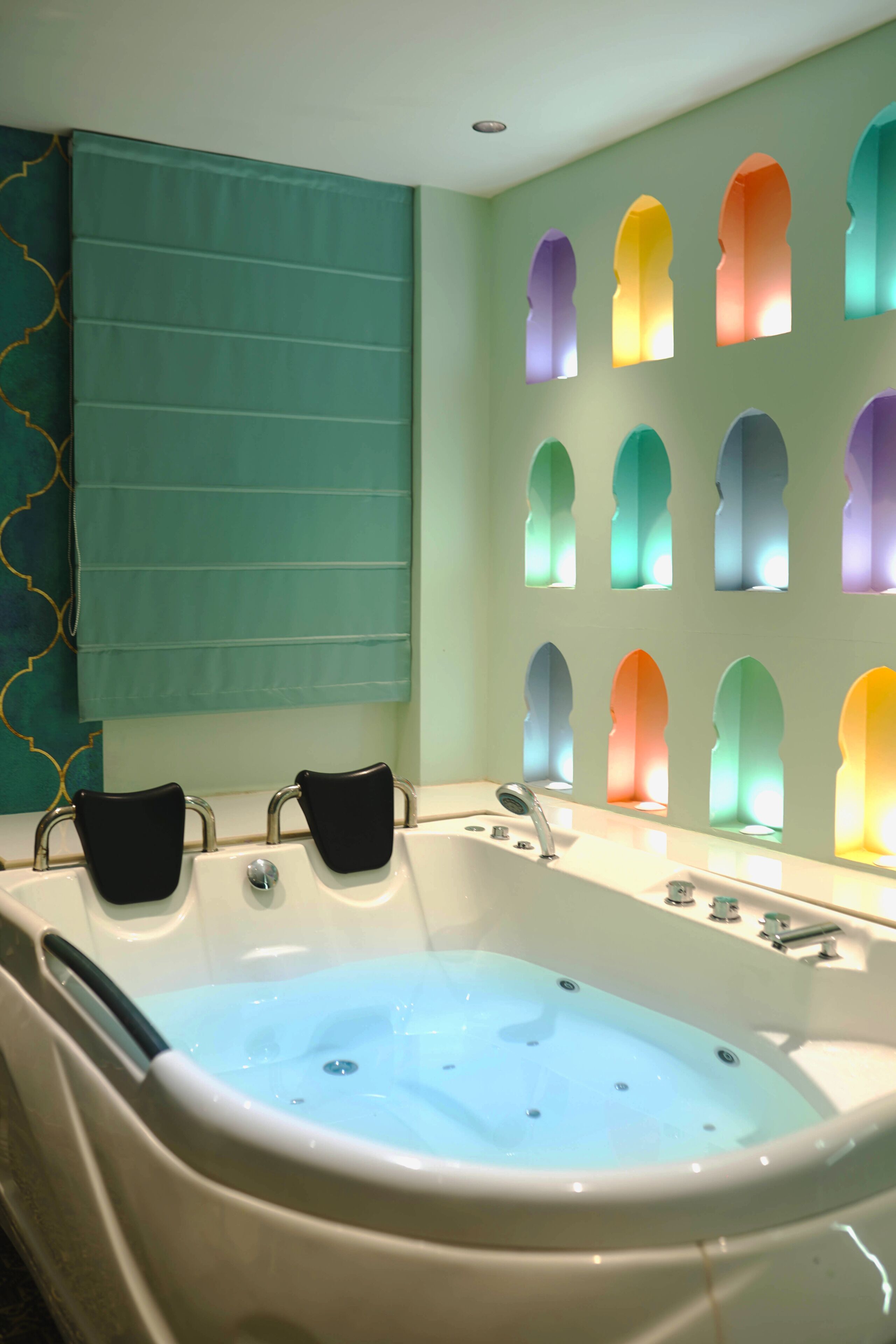 Une salle de bain avec une baignoire, deux serviettes noires et un mur orné de fenêtres en arc de cercle aux couleurs vives.