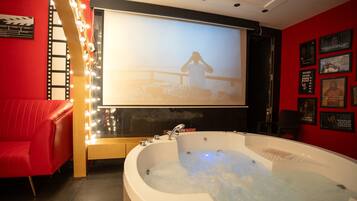 A room with a large bathtub, a red couch, and a wall with framed pictures.