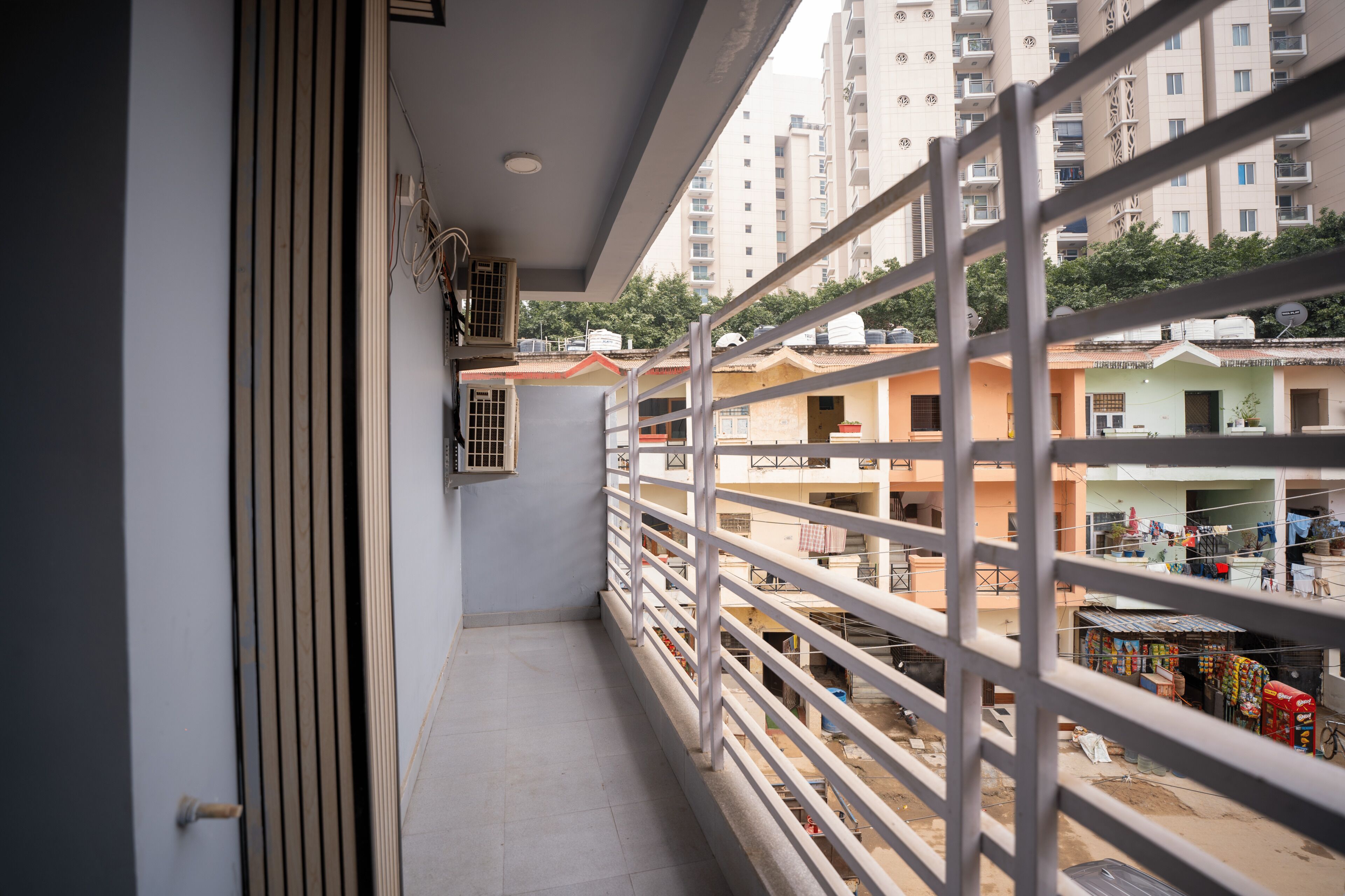 A narrow balcony with a metal railing overlooking a residential area with multi-story buildings.