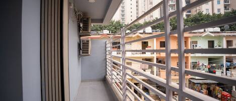 A narrow balcony with a metal railing overlooking a residential area with multi-story buildings.