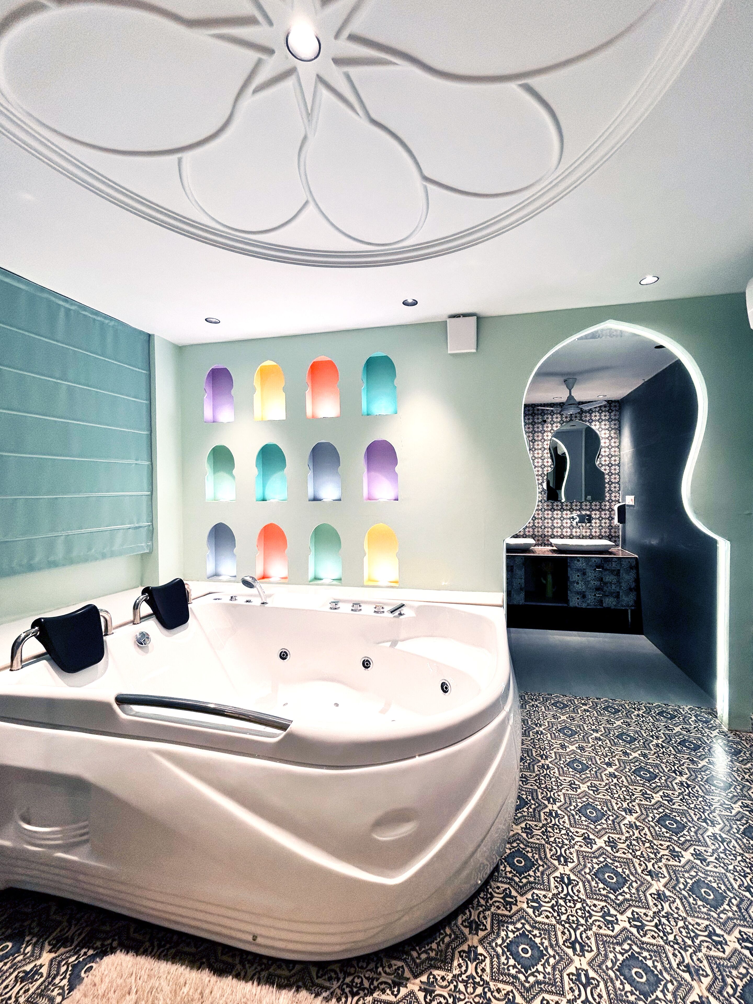A modern bathroom with a large bathtub, a patterned floor, and a unique wall design with illuminated arches.