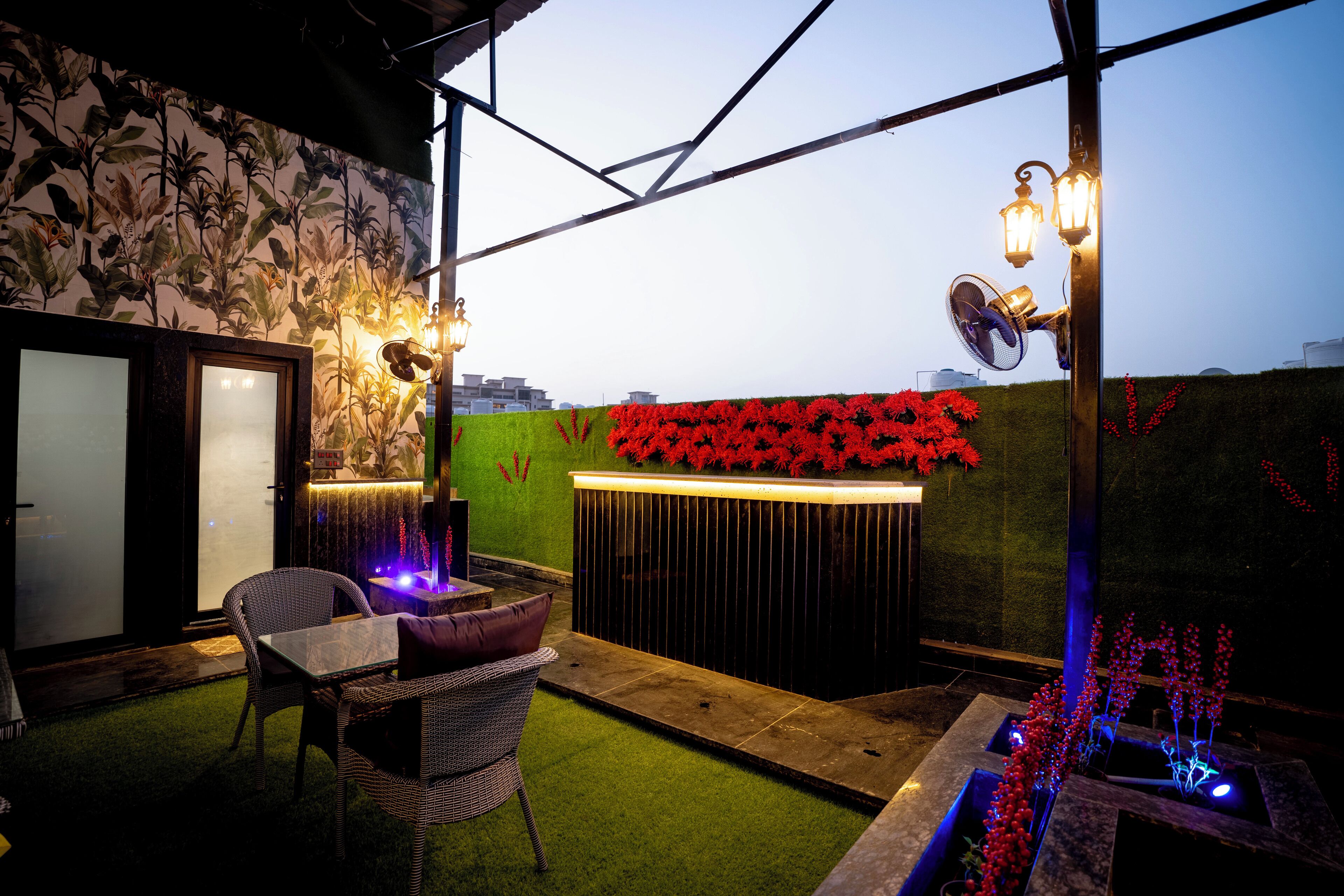 An outdoor patio area with a table and chairs, a decorative wall with red flowers, and a water feature.