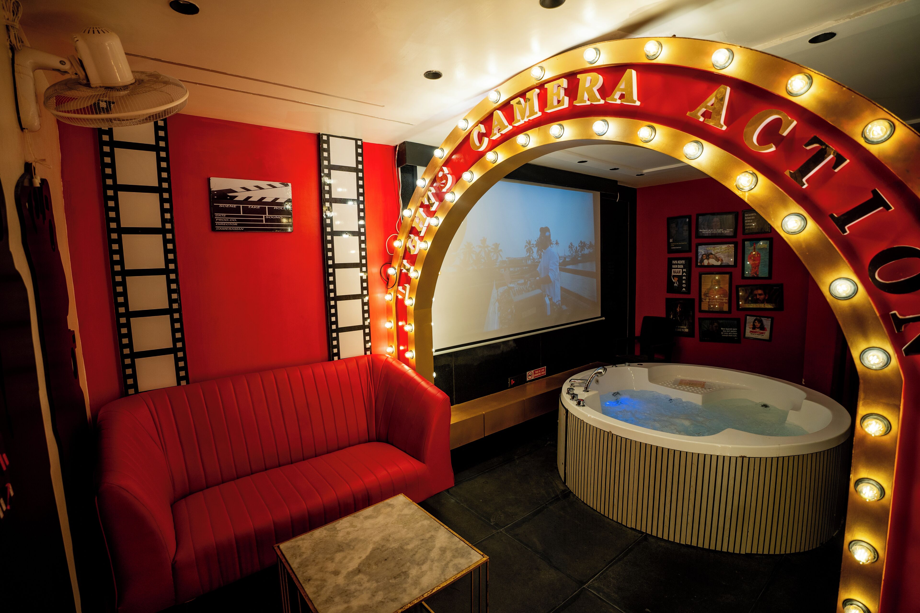A red cinema-themed room with a red sofa, a small table, a hot tub, and a large screen.