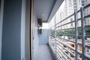 Un balcon étroit doté d’une rambarde en métal, d’un appareil de climatisation et offrant une vue sur un quartier résidentiel composé de plusieurs immeubles.