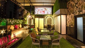 A cozy outdoor seating area with a flat-screen TV, comfortable wicker chairs, and a small table. - Orsom Stays Sassy - Sector 42 (Gurugram)