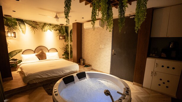 A modern bedroom with a large bed, a hot tub, and a kitchen area. - Orsom Stays Sassy - Sector 42 (Gurugram)