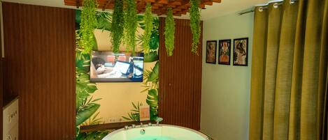 A bathroom with a wooden floor, a bathtub, and a wooden ceiling with hanging plants.