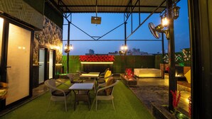 An outdoor patio with artificial grass, wicker furniture, and a bar area with a red flower arrangement. - Orsom Stays Sassy - Sector 42 (Gurugram)
