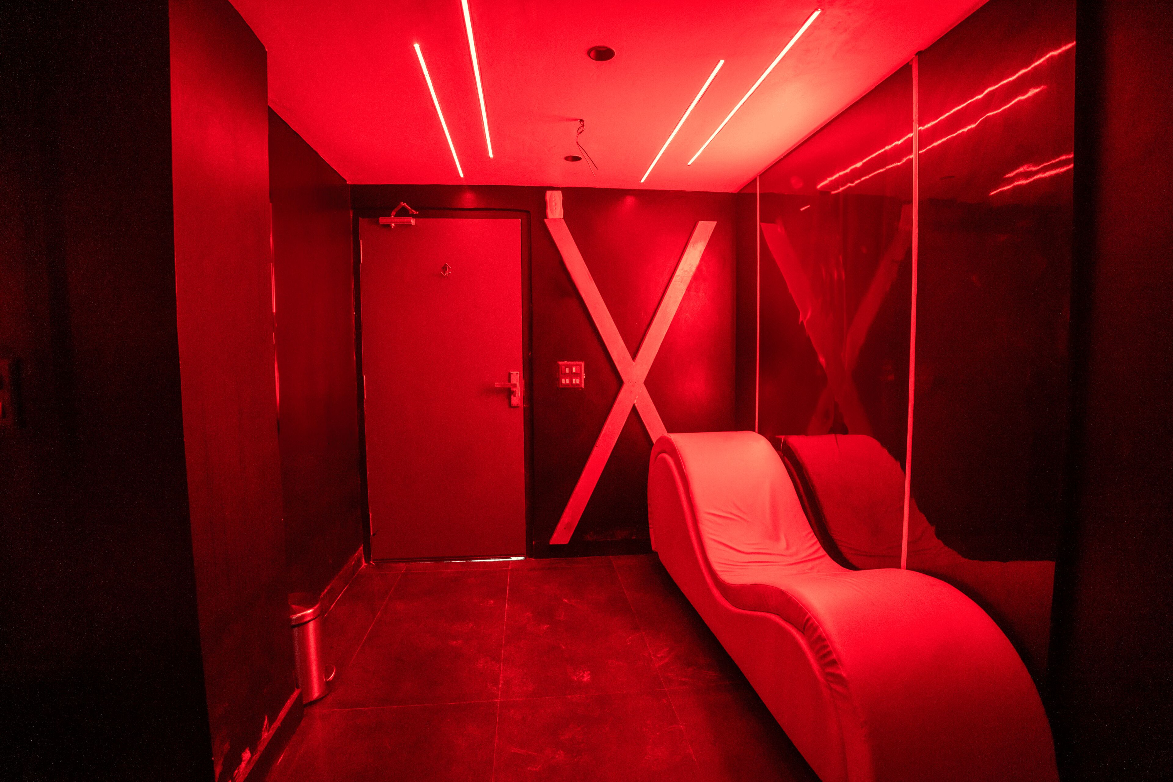 A red-lit room with a bed, a door, and a wall with a large 'X' design.