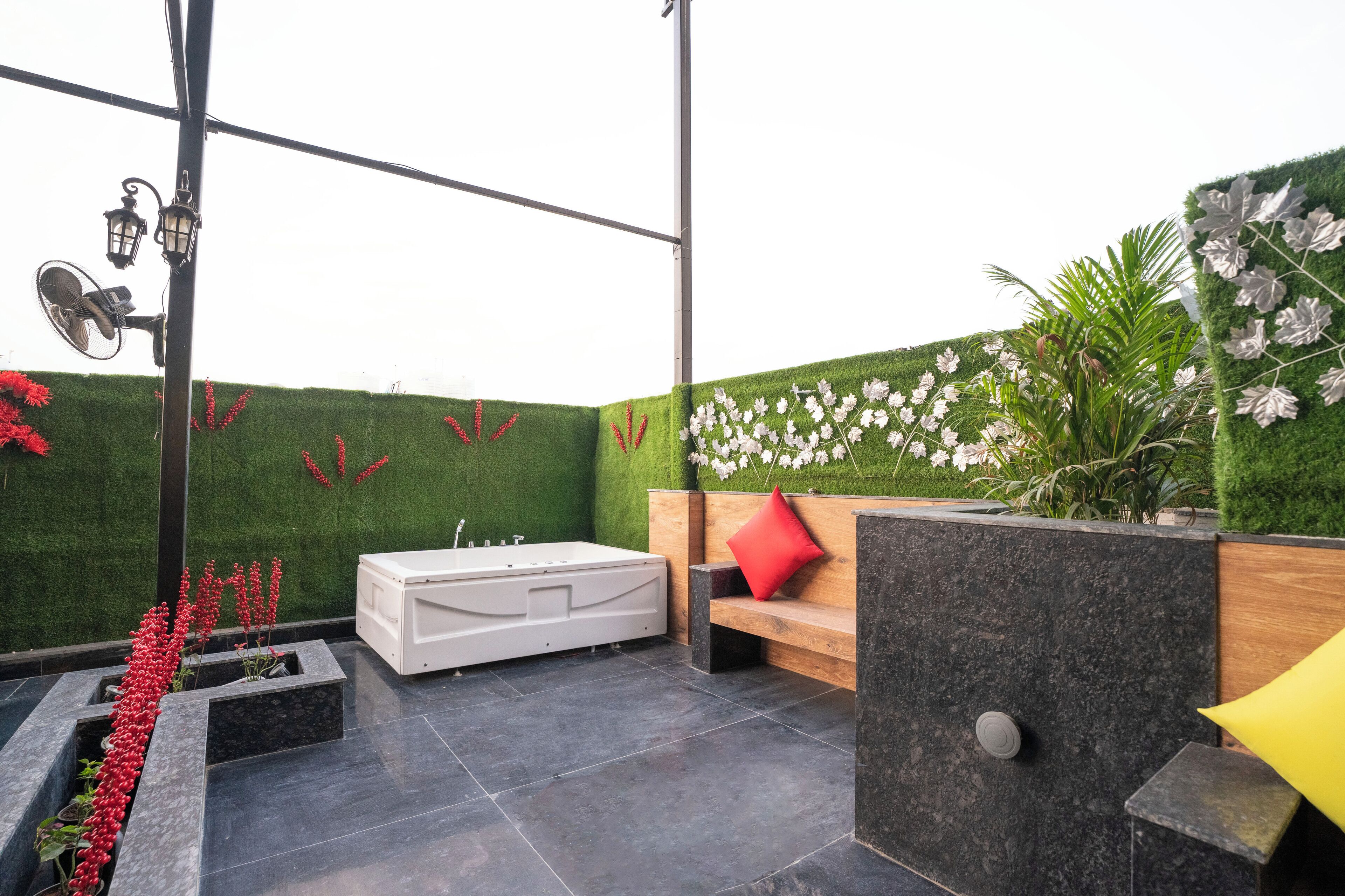 A modern outdoor bathroom with a freestanding bathtub, a bench, and a wall with artificial grass and flowers.