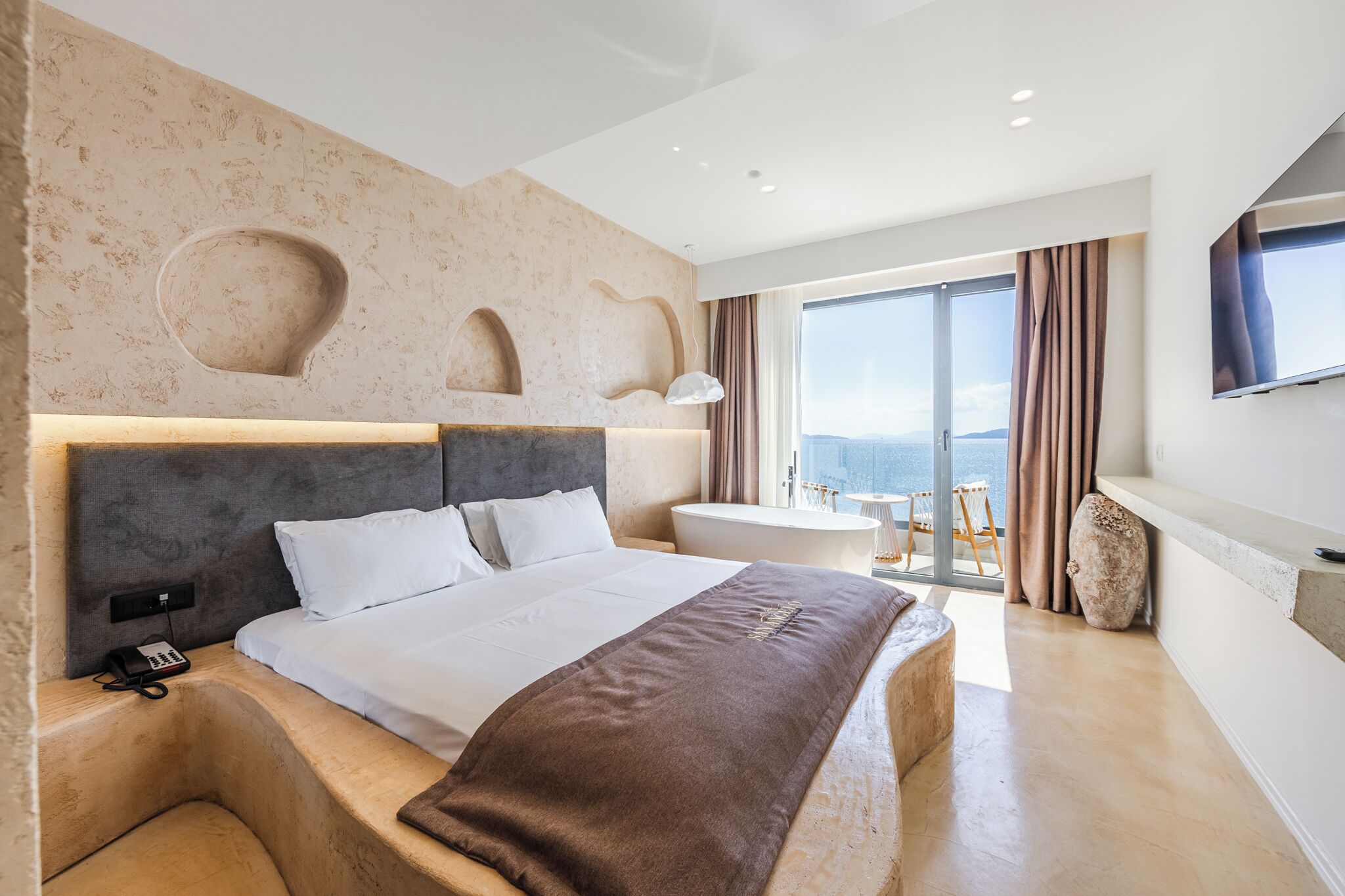 A modern hotel room with a large bed, a bathroom, and a balcony with a view.