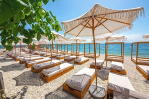 Een strand met rijen ligbedden en parasols, houten loungers en een helder uitzicht op de zee.