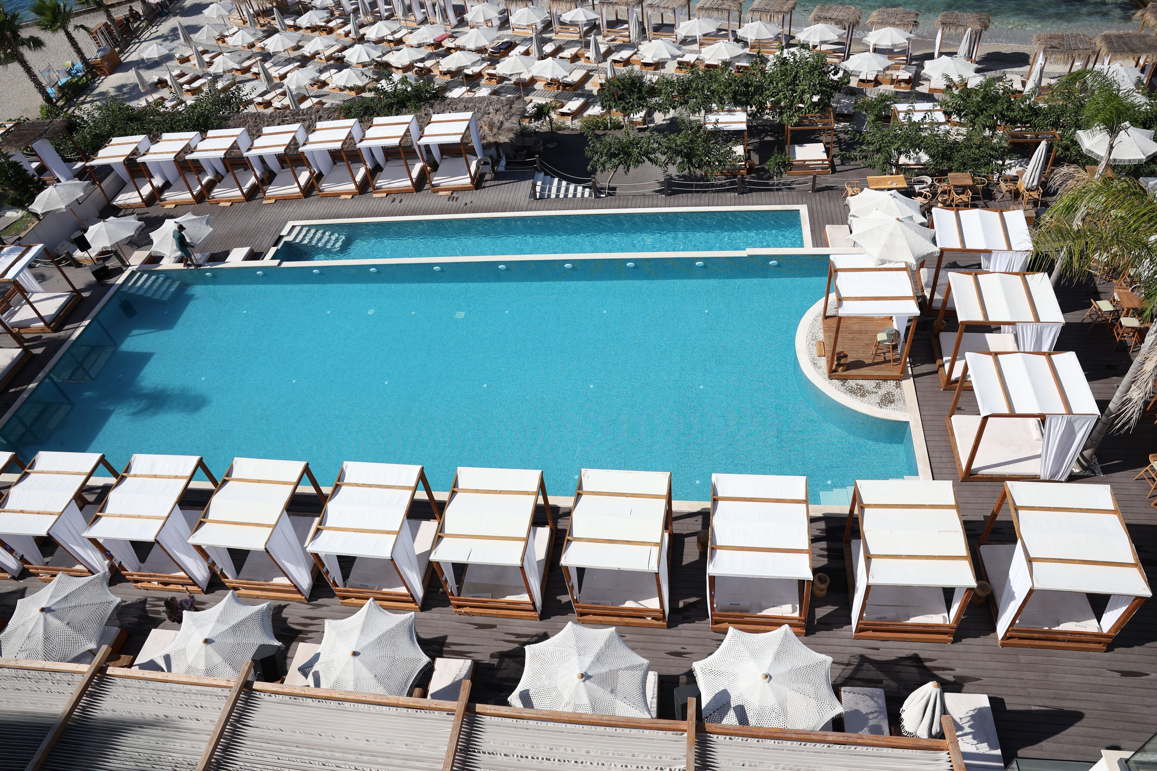 A large pool surrounded by numerous sun loungers and umbrellas, with a wooden deck and a clear blue pool.
