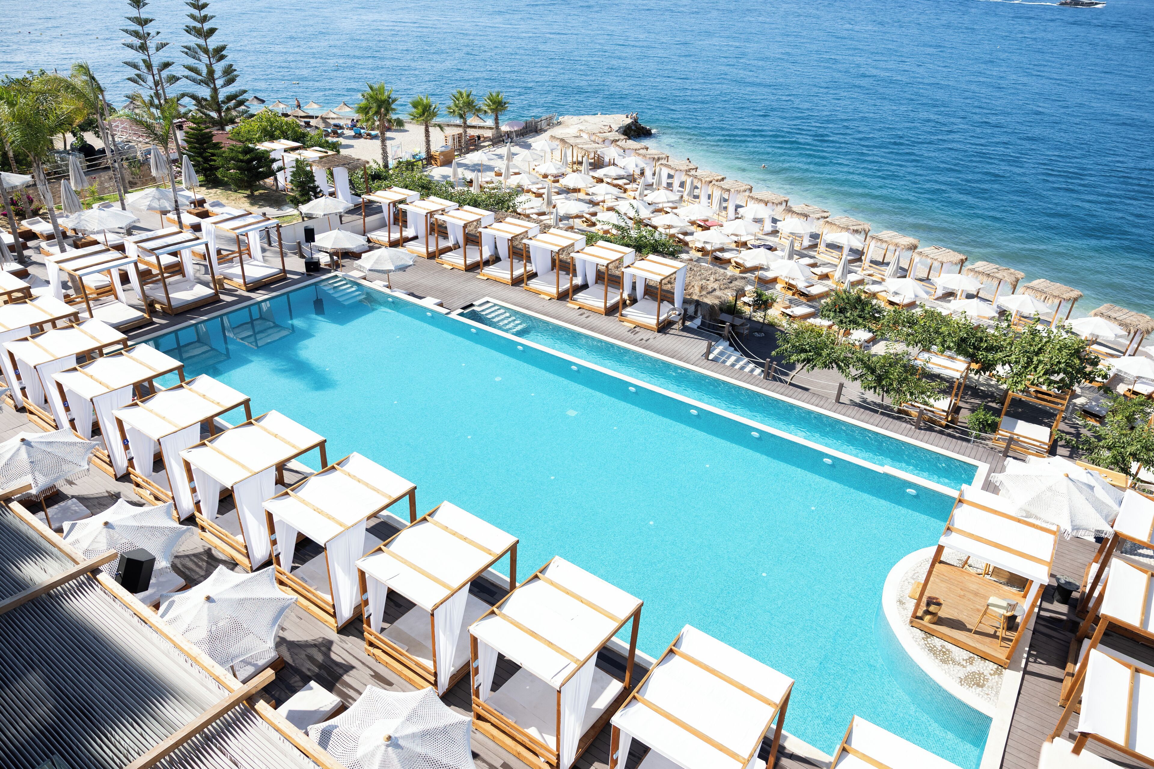 Ein großer Pool, umgeben von Liegestühlen und Sonnenschirmen, mit Blick aufs Meer.