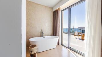 Un baño moderno con una bañera independiente, amplias puertas correderas de vidrio y vistas a un balcón con mobiliario exterior.