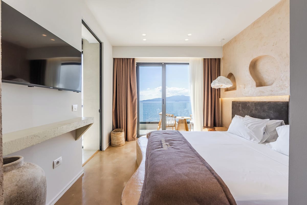 Een hotelkamer met een bed, een televisie, een groot raam en uitzicht op zee.