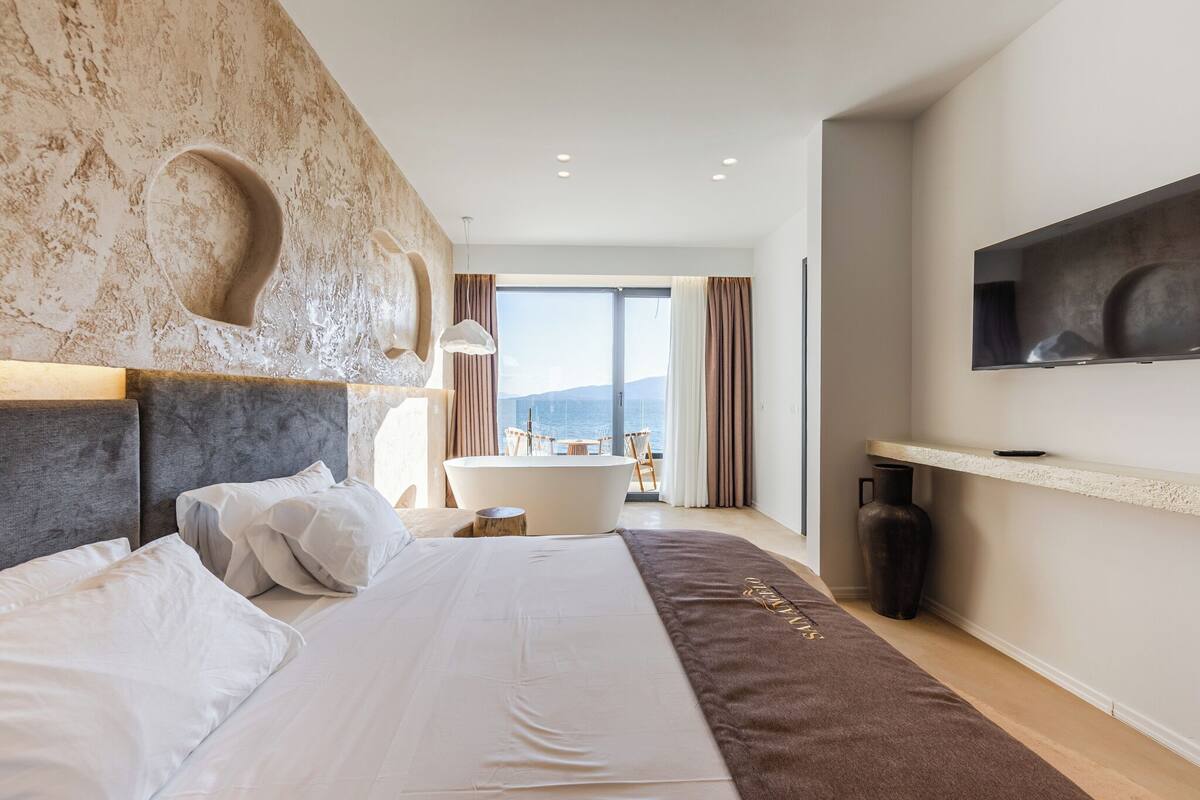 Een moderne hotelkamer met een groot bed, een badkuip, een flatscreen-tv en uitzicht op zee.