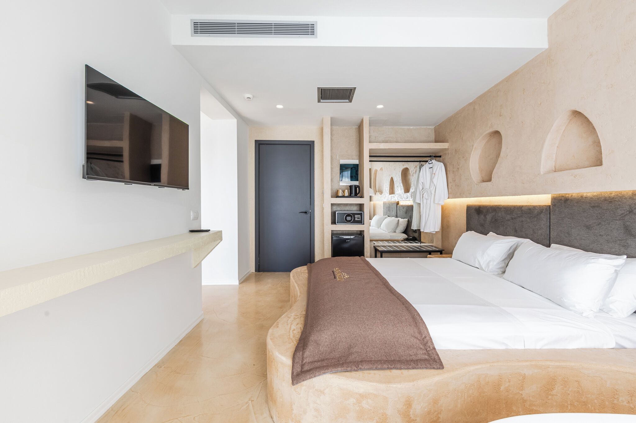 Een moderne hotelkamer met een groot bed, een aan de muur bevestigde televisie, een kledingkast en een badkamer die door een open deur zichtbaar is.
