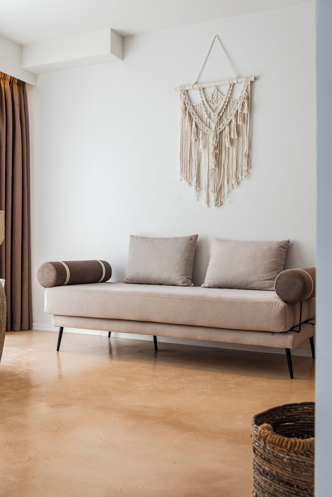 Un salón minimalista con un sofá en tonos neutros, un tapiz de macramé y una cesta tejida en el suelo.