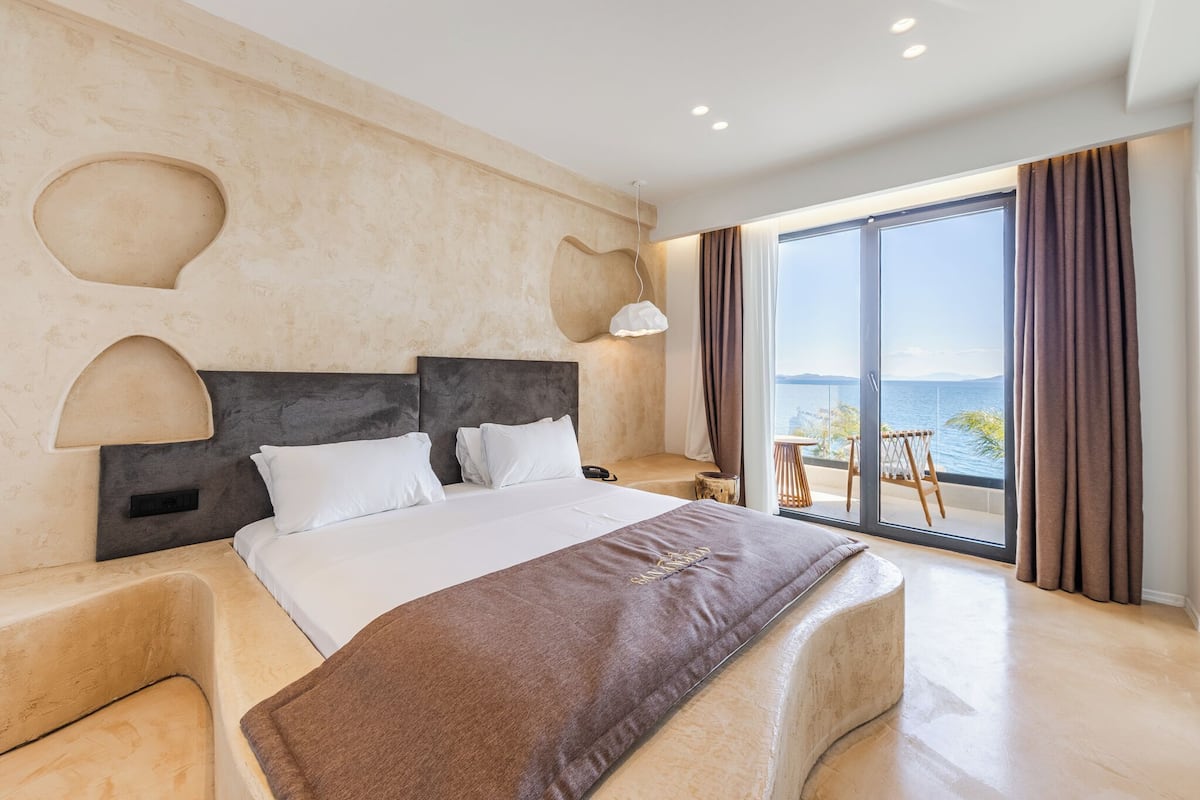 Een moderne hotelkamer met een groot bed, uitzicht op zee en een balkon met een stoel.