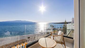 A balcony with a view of the sea and mountains, featuring wicker chairs and a small table.