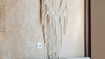 A room with a textured beige wall, a macrame wall hanging, a beige sofa, and a small wooden table.